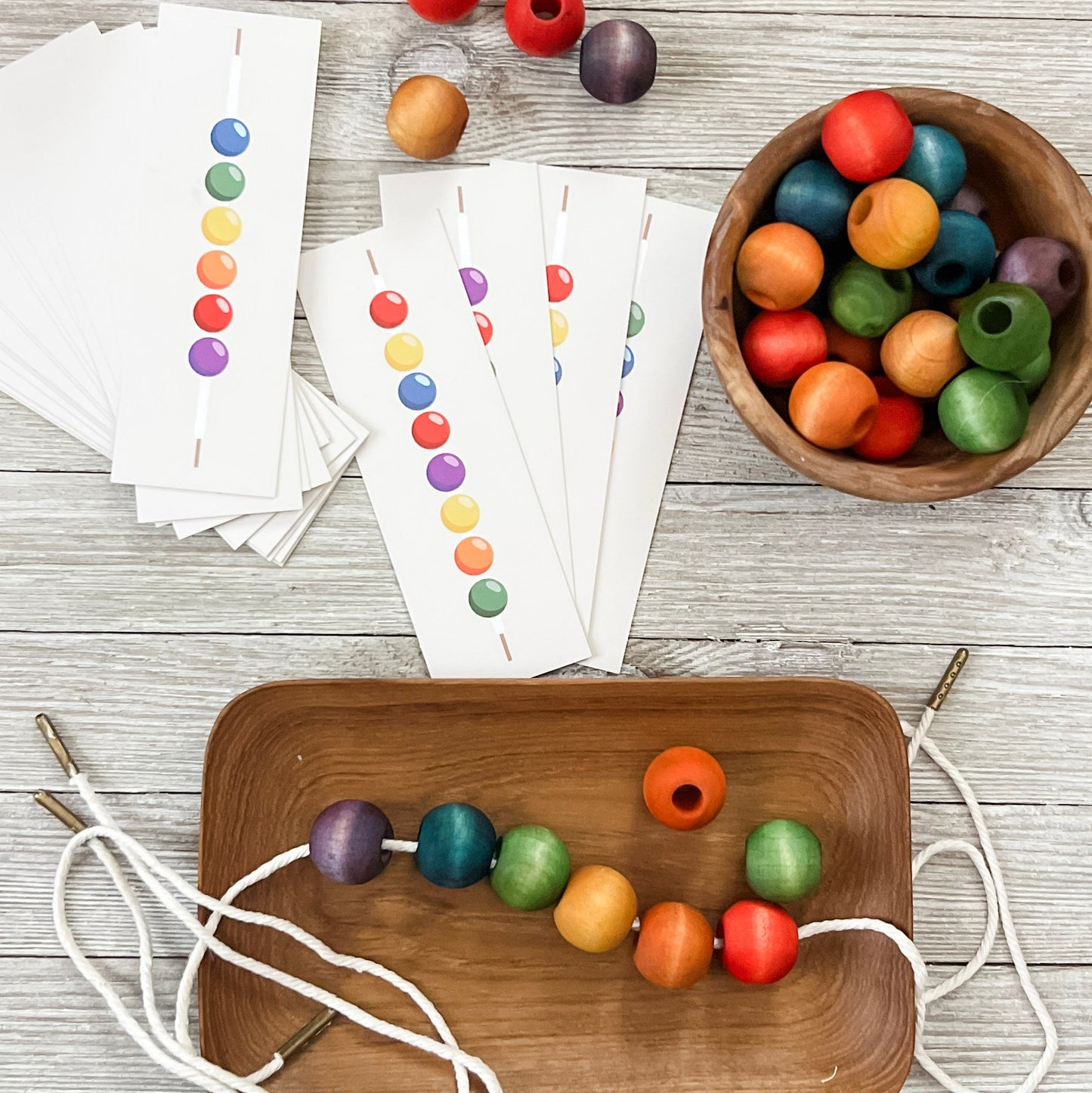 Colorful wooden beads on a wooden tray with cards and more beads in the background.
