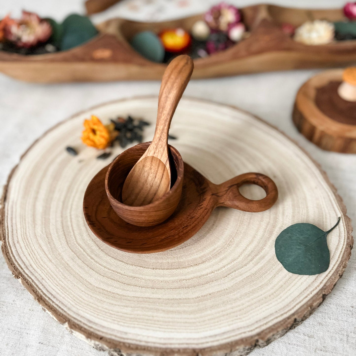 Wooden spoon and cup on a round woven mat with a white background