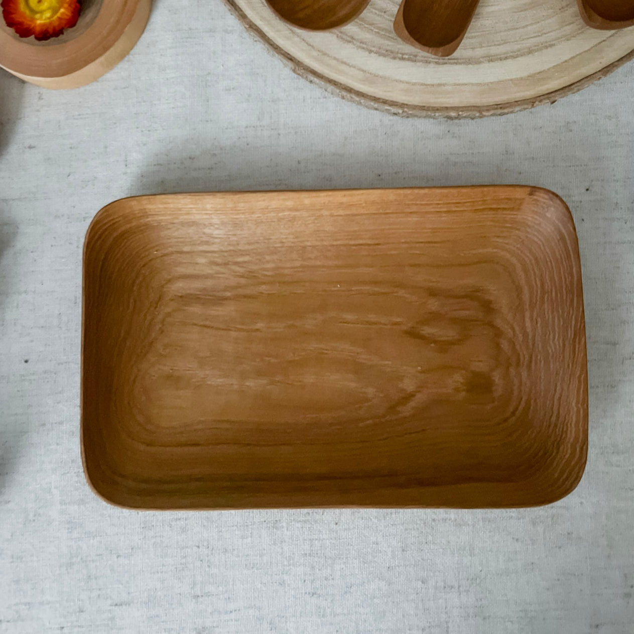 Wooden kitchen utensils including a rectangular plate, spoons, and measuring cups on a light surface.