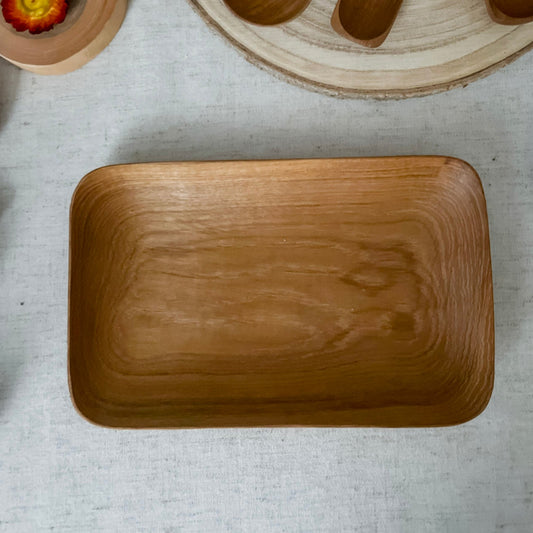 Wooden kitchen utensils including a rectangular plate, spoons, and measuring cups on a light surface.