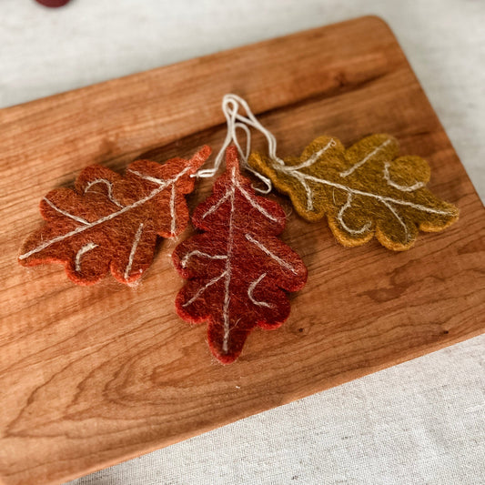 Felt leaf decorations on a wooden board with a neutral background