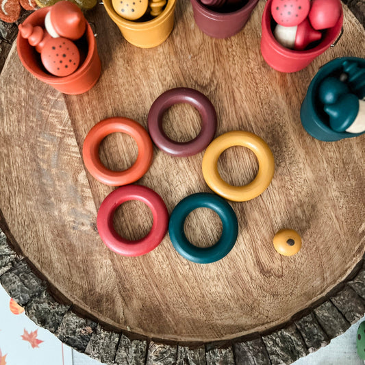 Colorful wooden rings on a rustic wooden surface with small containers filled with items.