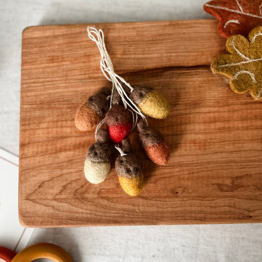 Wooden cutting board with felted autumn decorations on a light background
