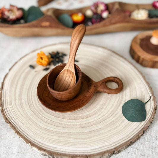 Wooden spoon and cup on a round woven mat with a white background