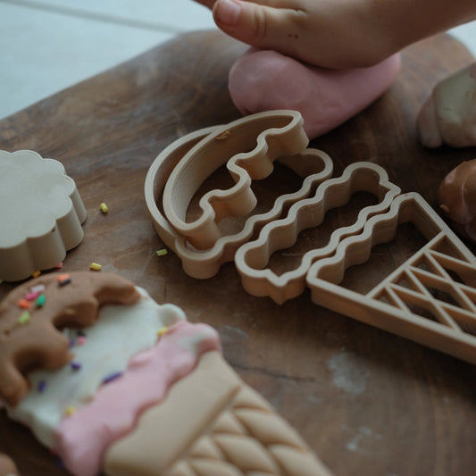 Cookie cutters shaped like ice cream cones and other shapes on a wooden board with cookies.