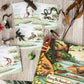 A children's nature-themed book and matching cards laid out on a light wood surface, surrounded by small animal figurines, dried leaves, and branches. The book cover shows a colorful riverbank scene with animals, and the cards show illustrated animals in circular frames.